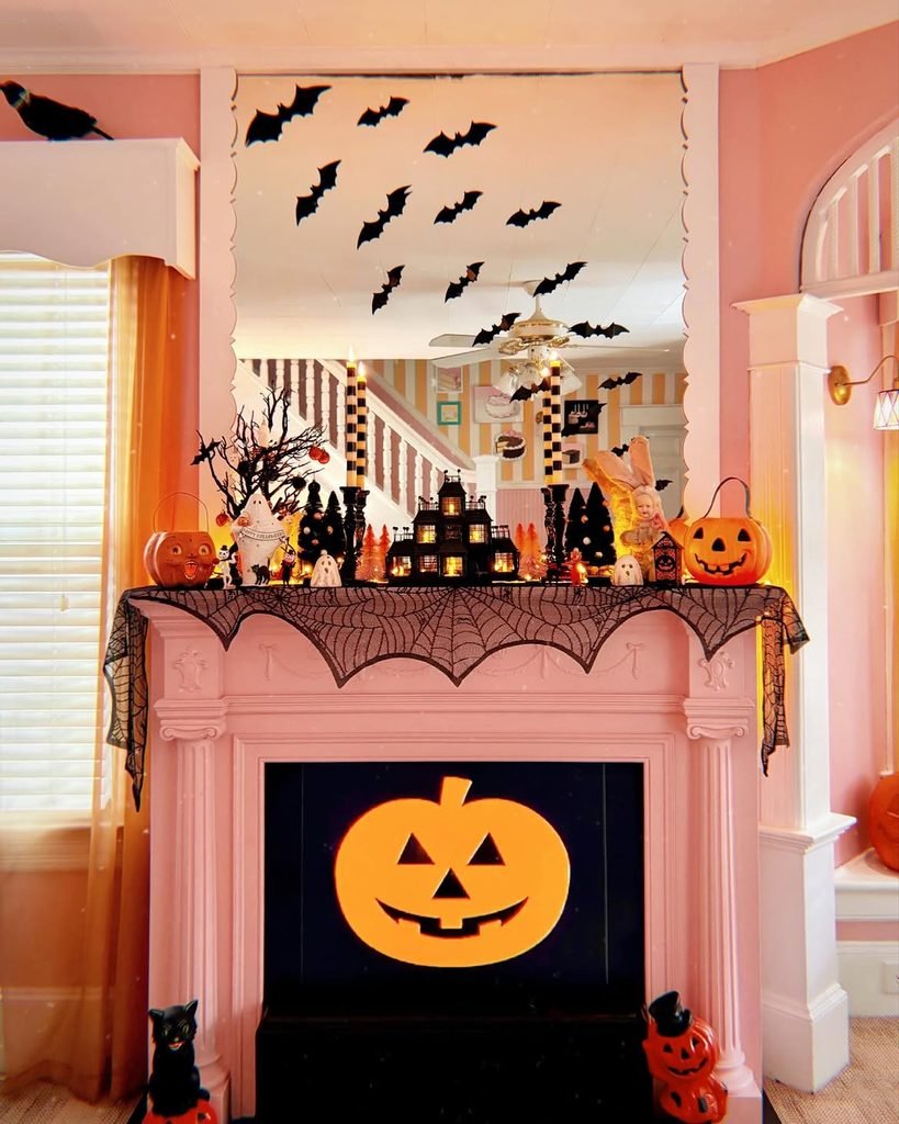pink fireplace mantle decorated with paper bats, miniature halloween houses, and jack-o-lantern