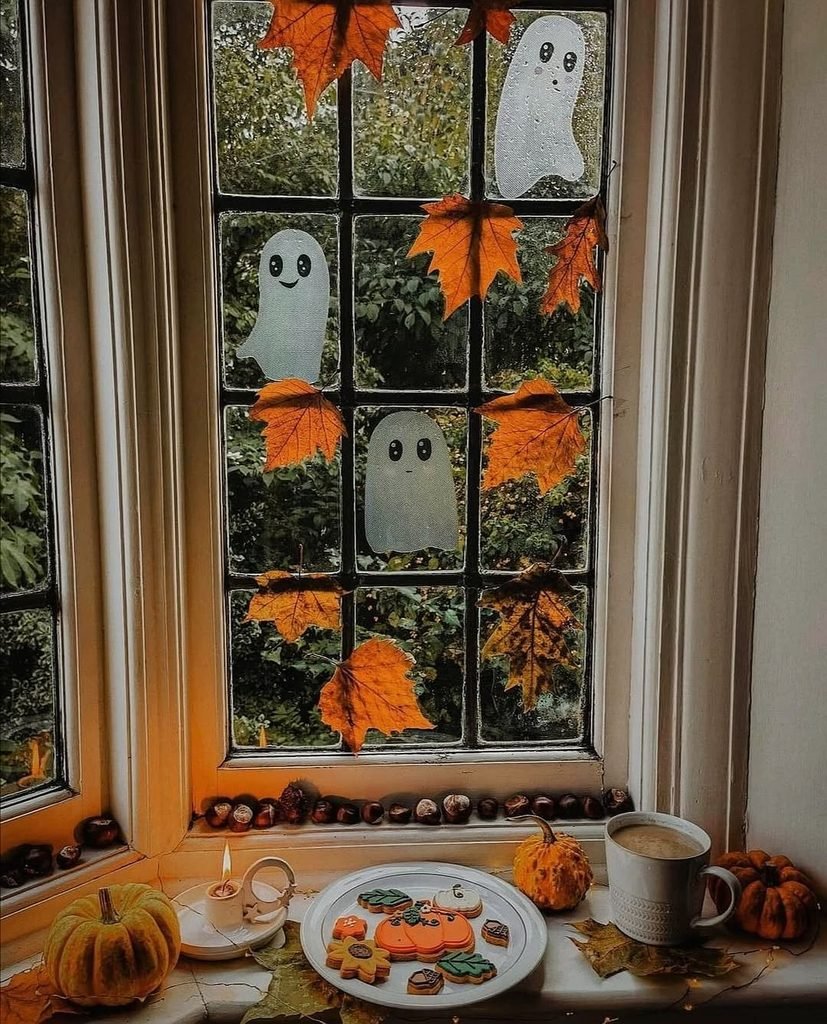 autumn window sill decorated with ghost decals, leaves, cookies, and coffee
