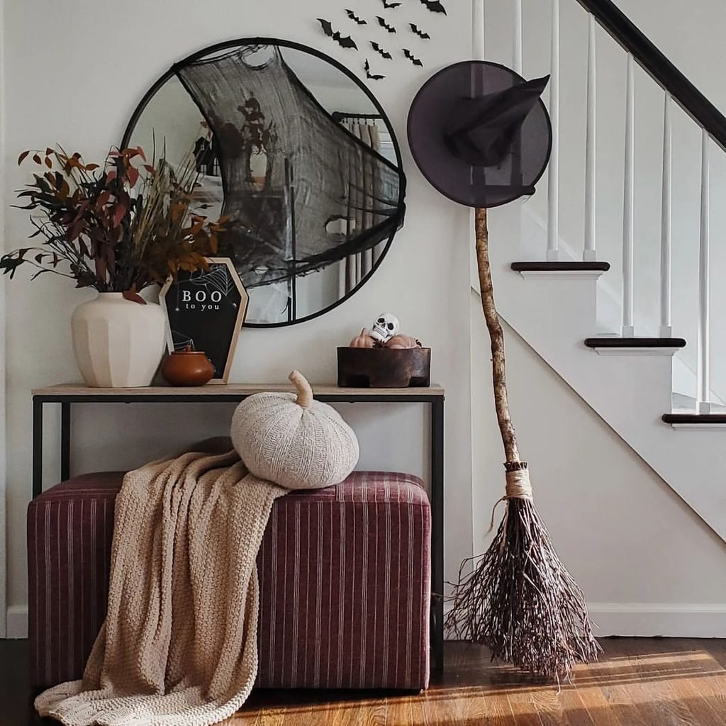 hallway console table decorated with a broom, mirror, bat decals, and pumpkin