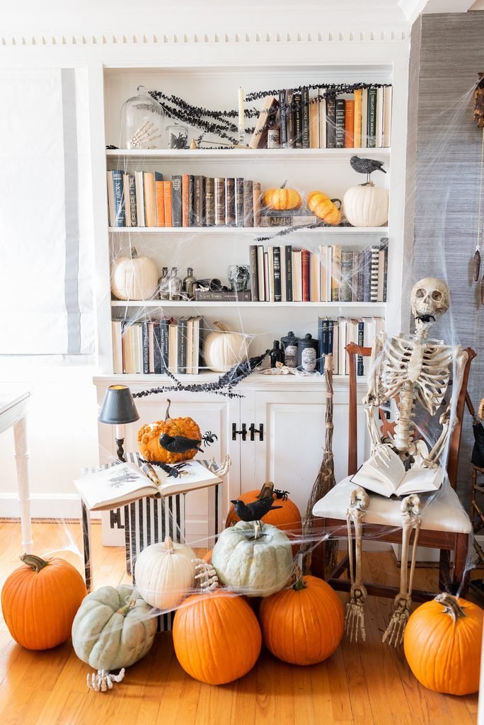bookshelf decorated with spiderwebs, pumpkins, and a reading skeleton in a chair