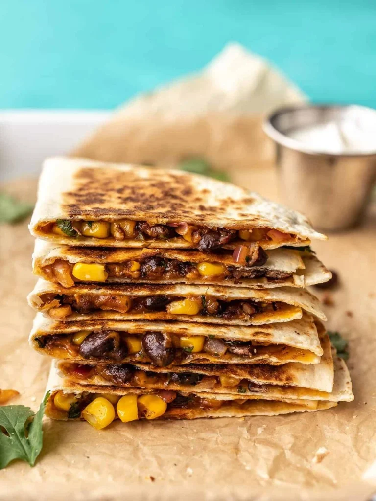 stack of crispy black bean and corn quesadillas on parchment paper with dipping sauce