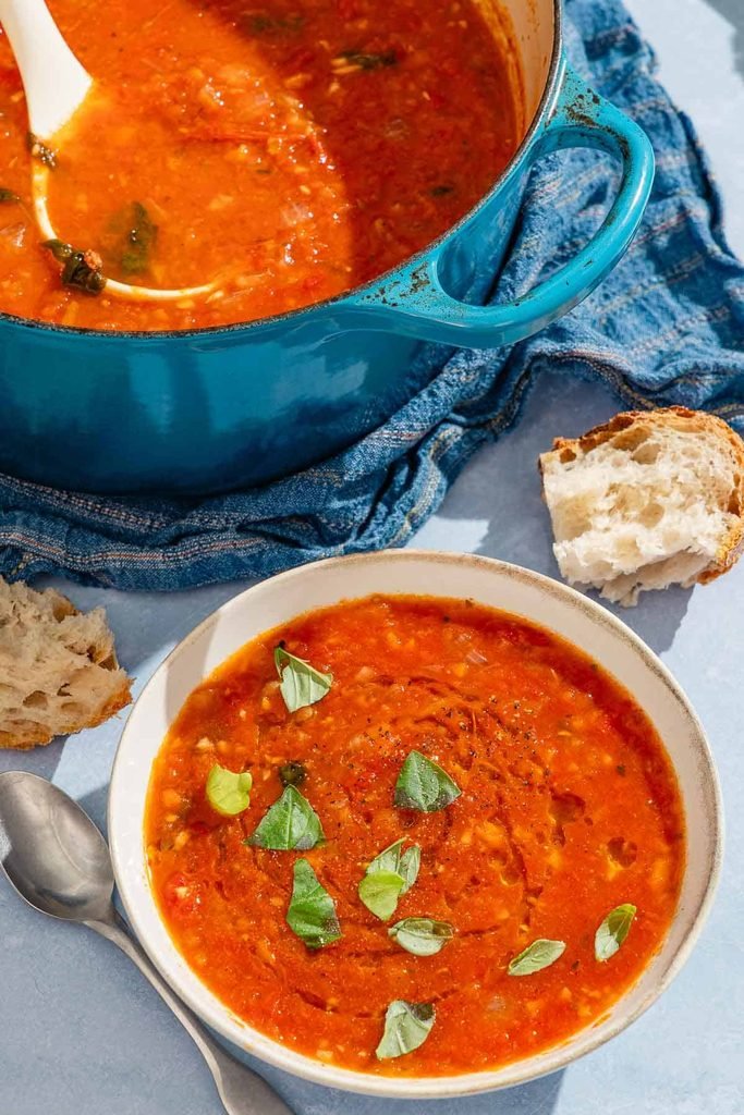 white bowl of red tomato basil soup served with crusty bread slices
