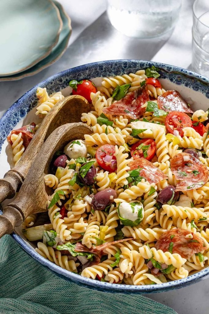 rotini pasta salad with salami, olives, cherry tomatoes, and mozzarella in a bowl