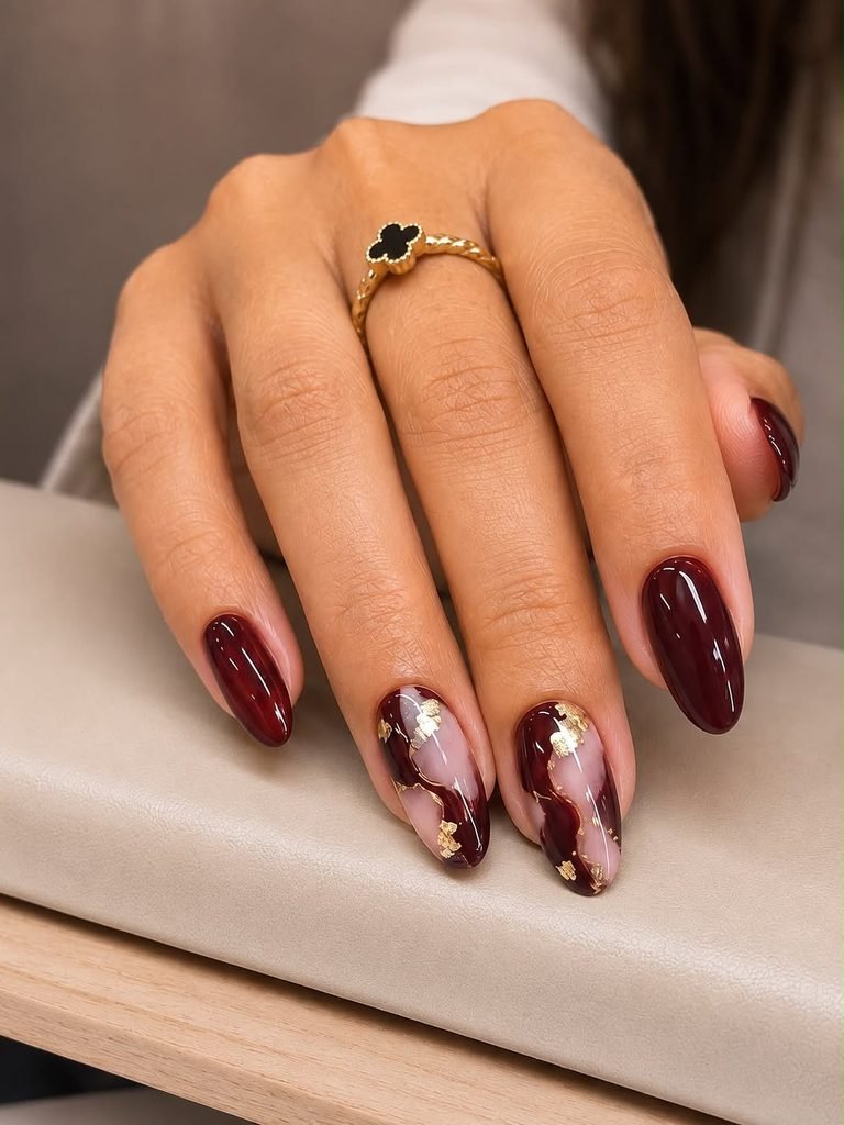 deep burgundy almond nails featuring two marble accent nails with gold foil flakes   