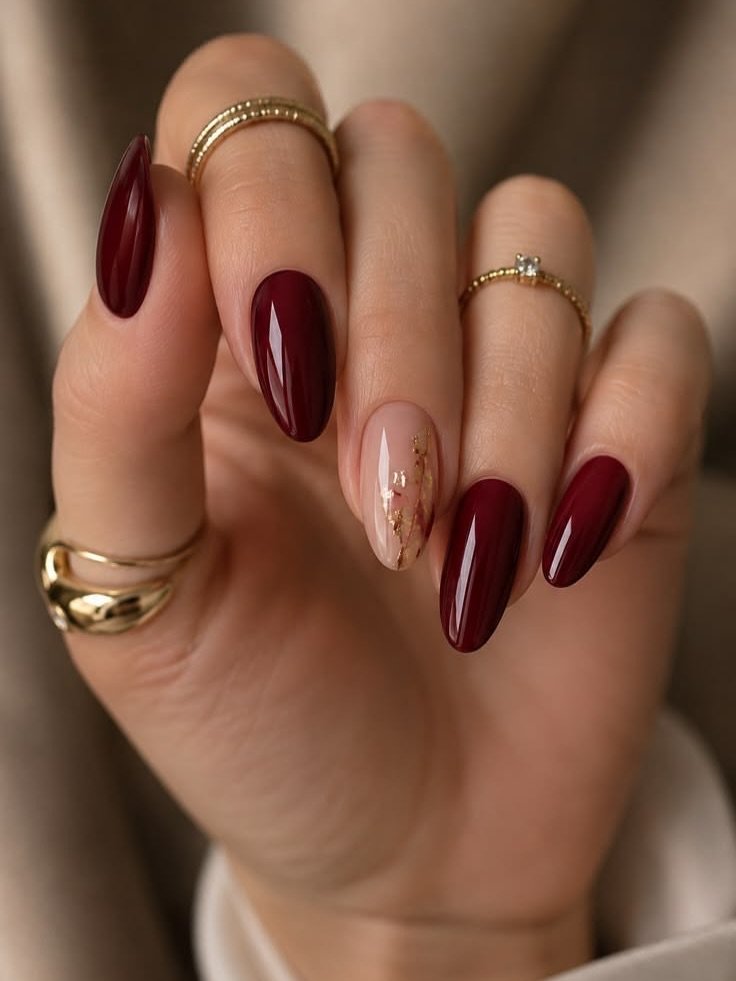 deep burgundy glossy almond nails featuring one nude accent nail with gold foil   