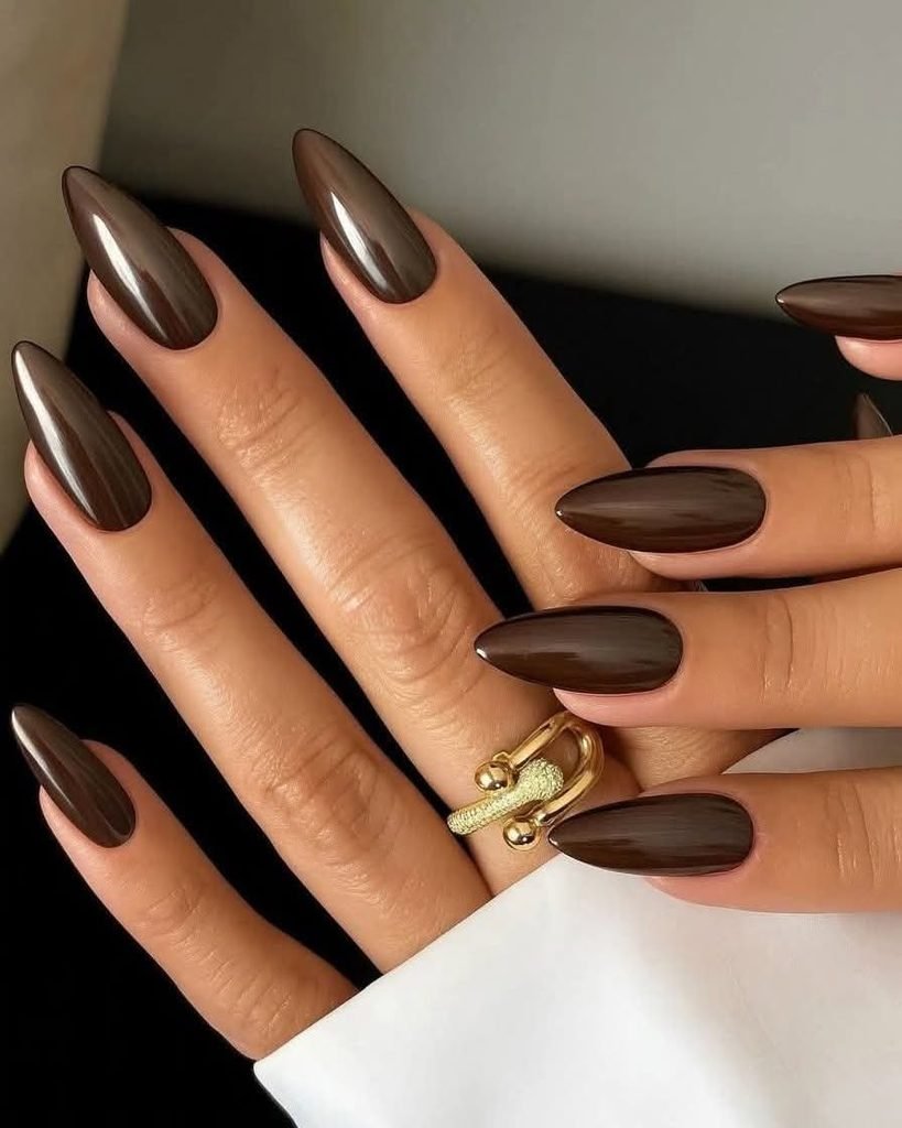 glossy dark chocolate brown almond nails styled with a gold ring   