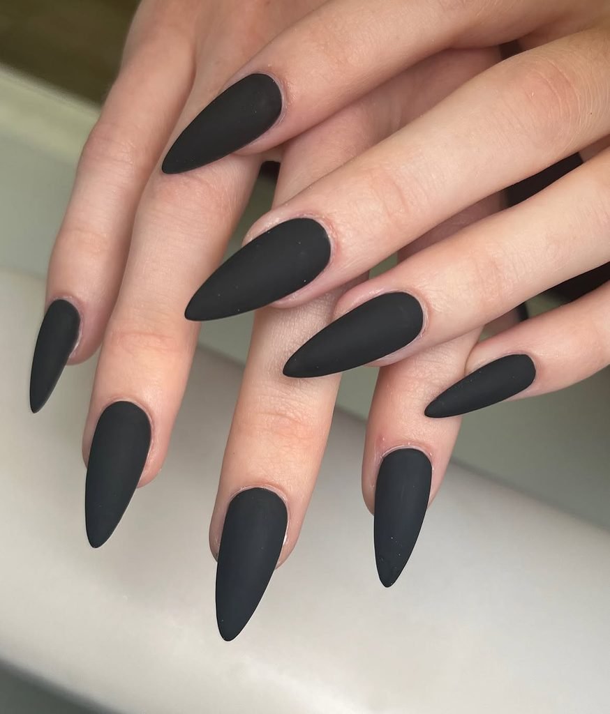 long matte black stiletto nails shown on a hand with pointed tips   