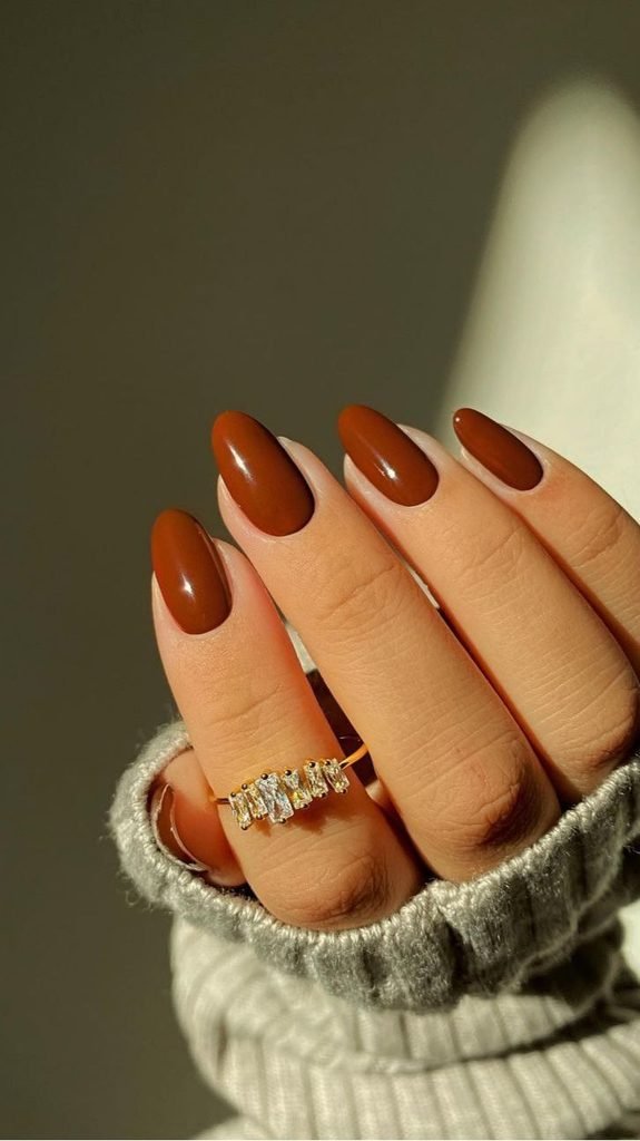 warm rust brown glossy almond nails paired with a gold gemstone ring   