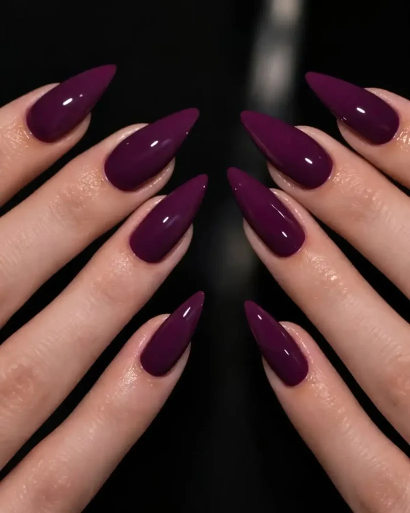glossy deep plum purple stiletto nails displayed against a dark background   