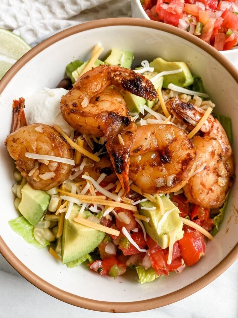 grilled shrimp taco bowl topped with avocado, shredded cheese, pico de gallo, and rice