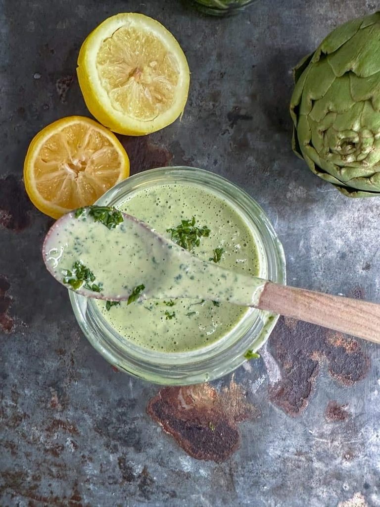 glass jar filled with green herbed tahini dressing topped with herbs and lemon slices