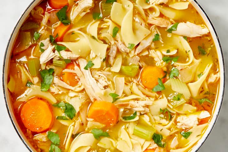 pot of warm chicken noodle soup with wide egg noodles and sliced carrots