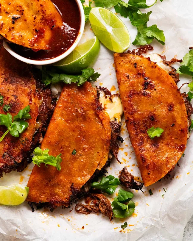 crispy birria tacos filled with melted cheese and shredded meat alongside dipping sauce   