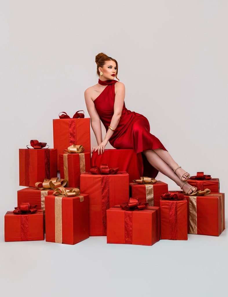 glamorous woman in a red dress sitting on a pile of wrapped gifts   