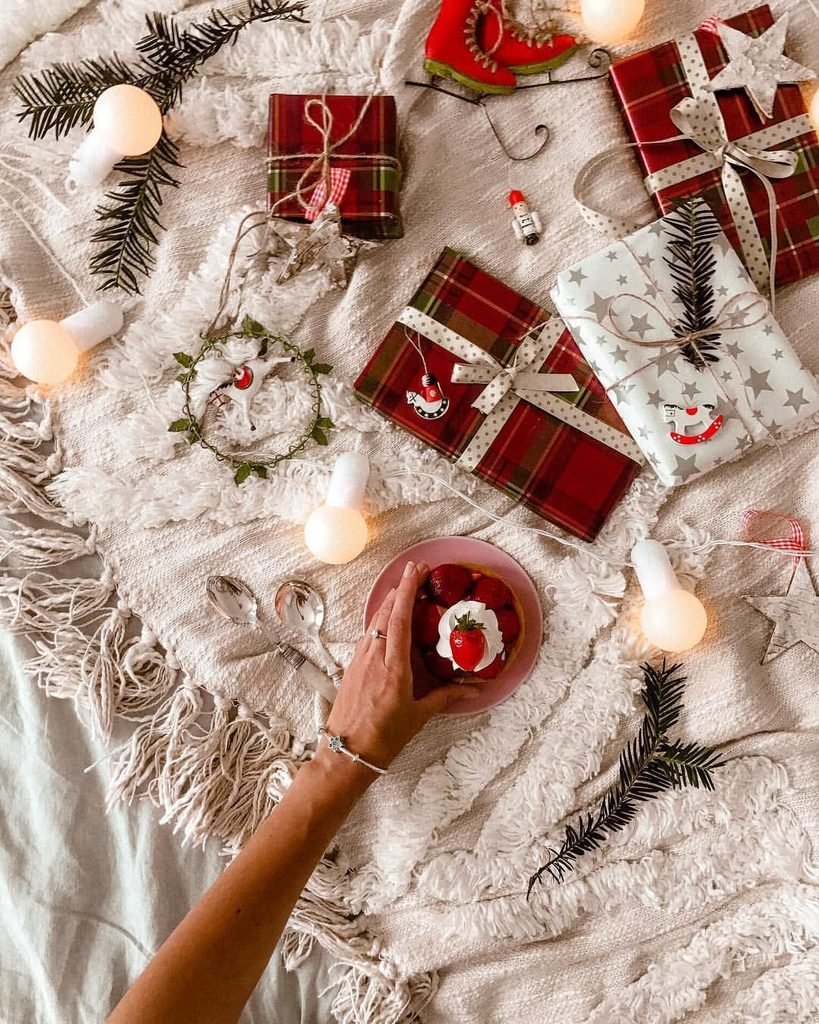 hand reaching for a strawberry dessert among wrapped christmas gifts on a cozy blanket   