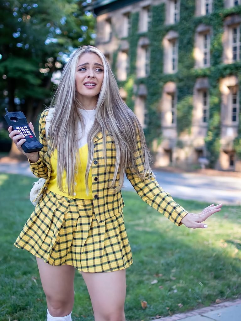 woman dressed in a yellow plaid cher horowitz outfit holding a vintage cell phone