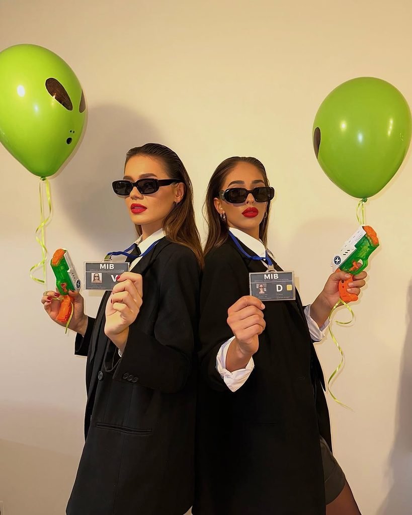two women in men in black costumes holding alien balloons, toy guns, and agent badges