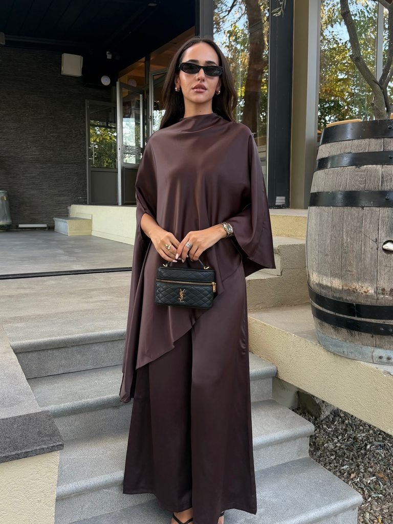 woman in a dark brown satin cape sleeve top and matching trousers