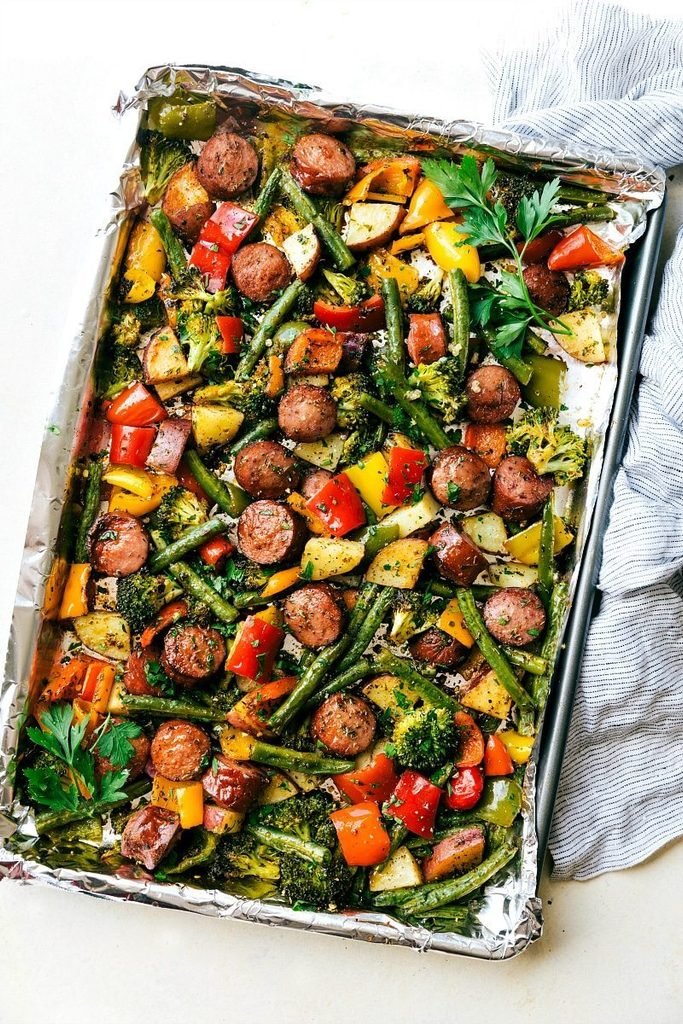 sheet pan sliced sausage with roasted broccoli, potatoes, and bell peppers on foil   