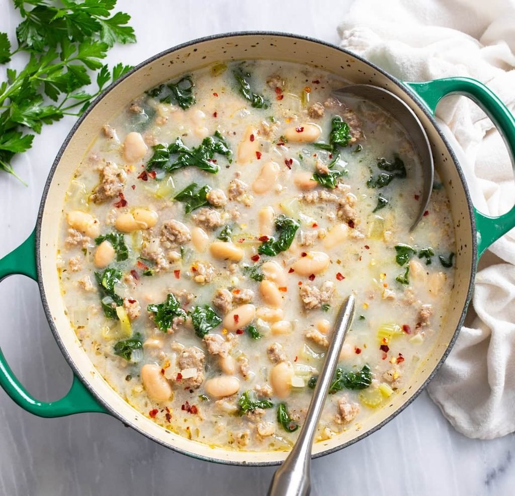 sausage and white bean soup with kale simmering in a green dutch oven   