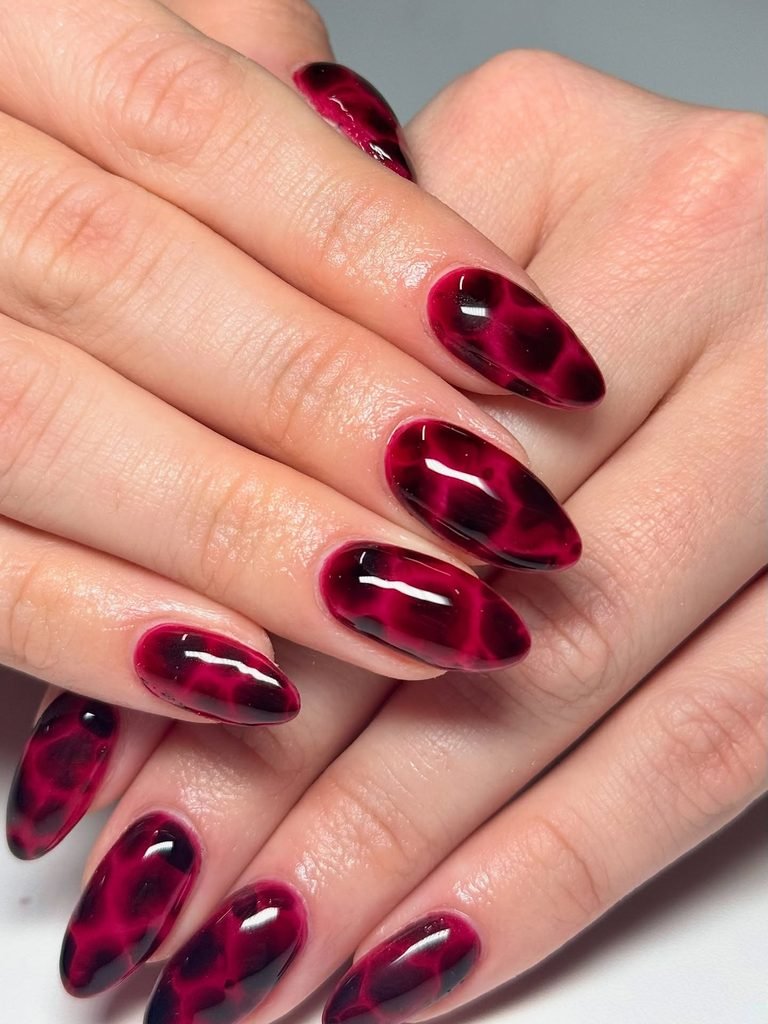 glossy dark red manicure with black tortoiseshell print on almond nails