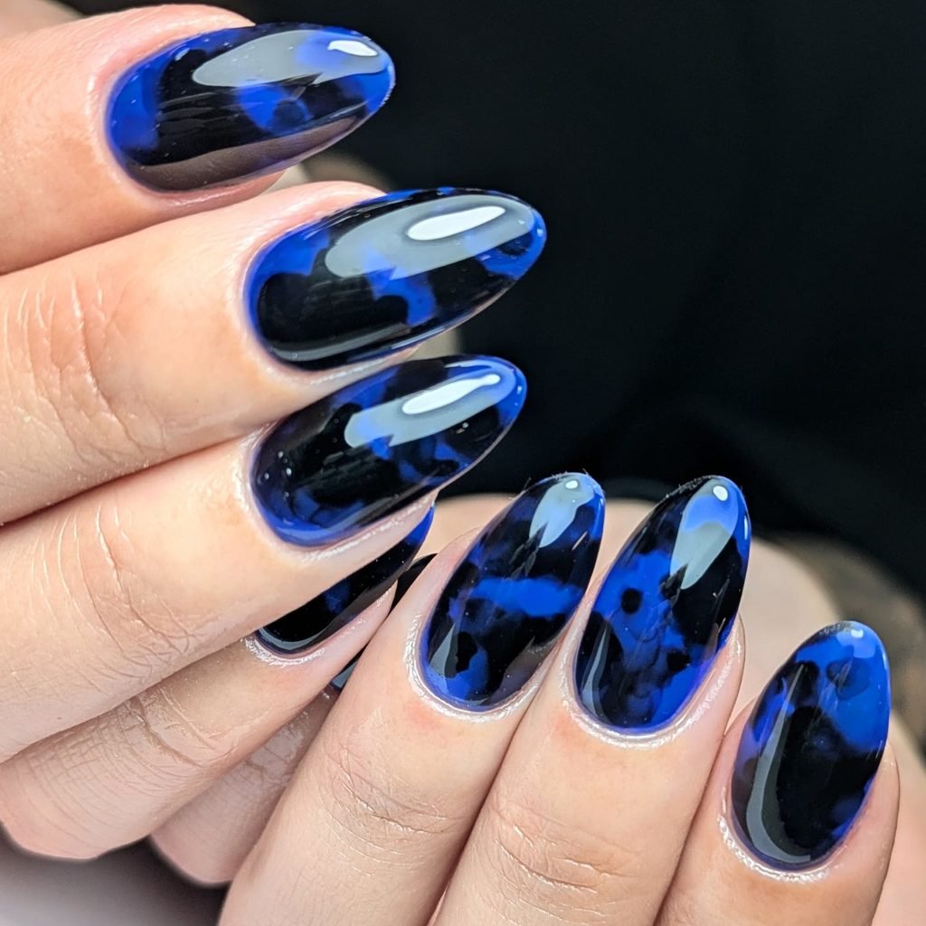 glossy black and vibrant blue marble pattern gel manicure on oval nails