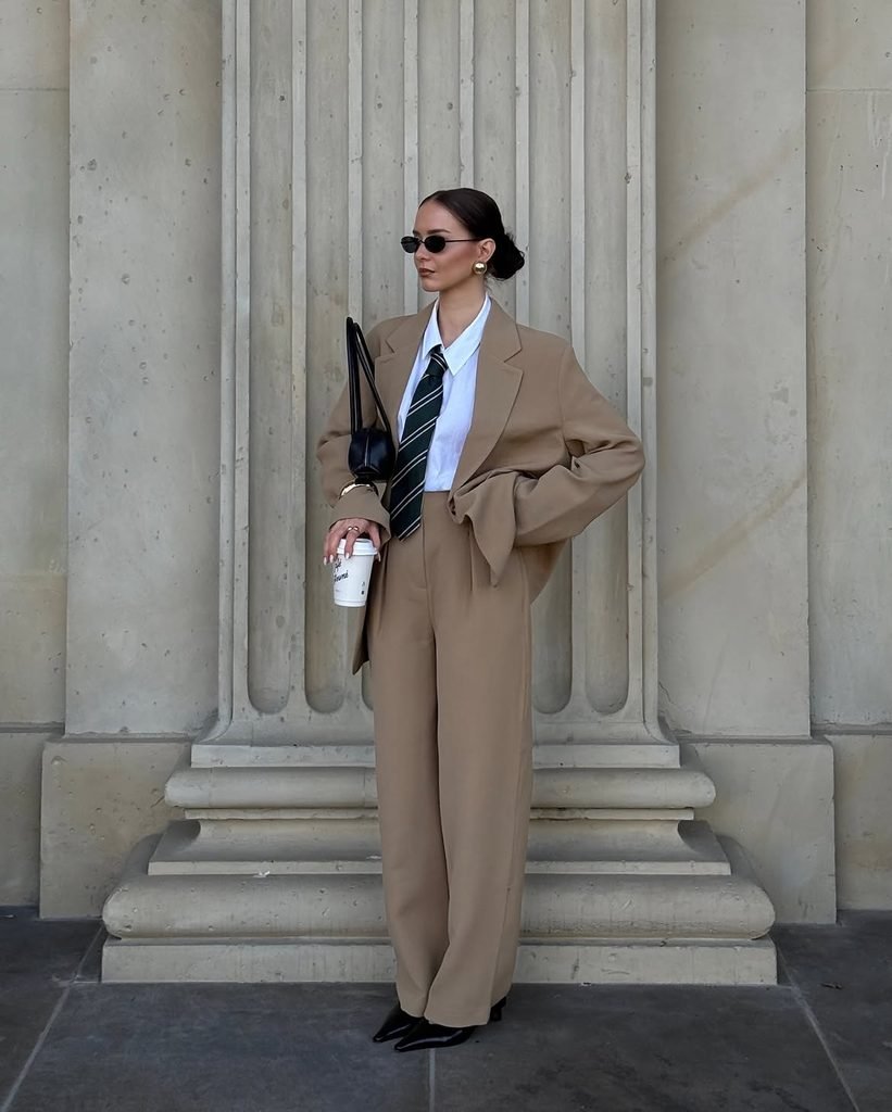 woman wearing an oversized beige suit, white collared shirt, and green tie