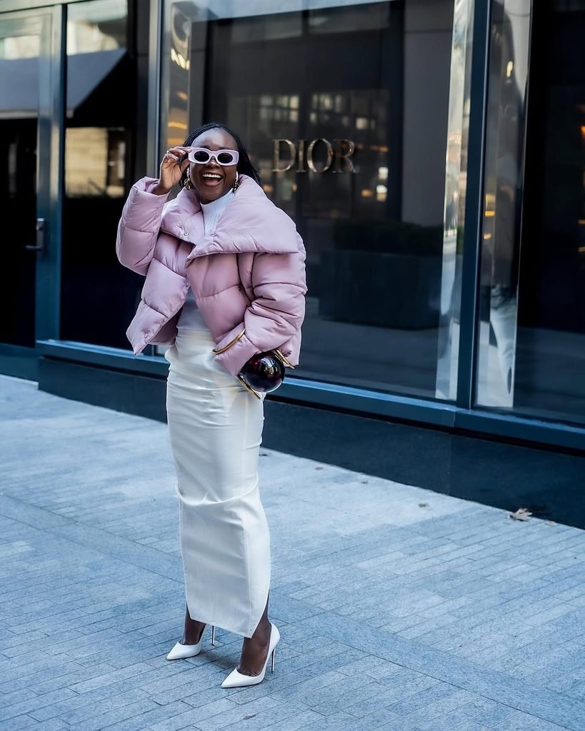 woman wearing a pink puffer jacket, white maxi skirt, and white heels