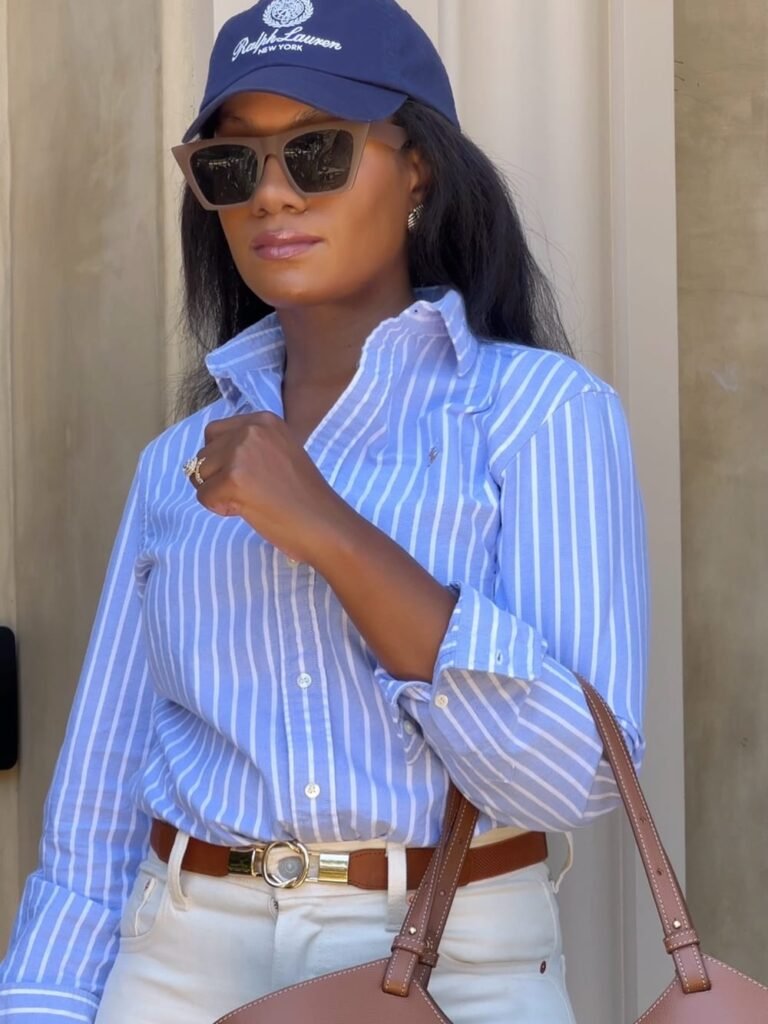 Blue-and-white striped button-down shirt with white jeans, a brown belt, navy cap and taupe handbag.