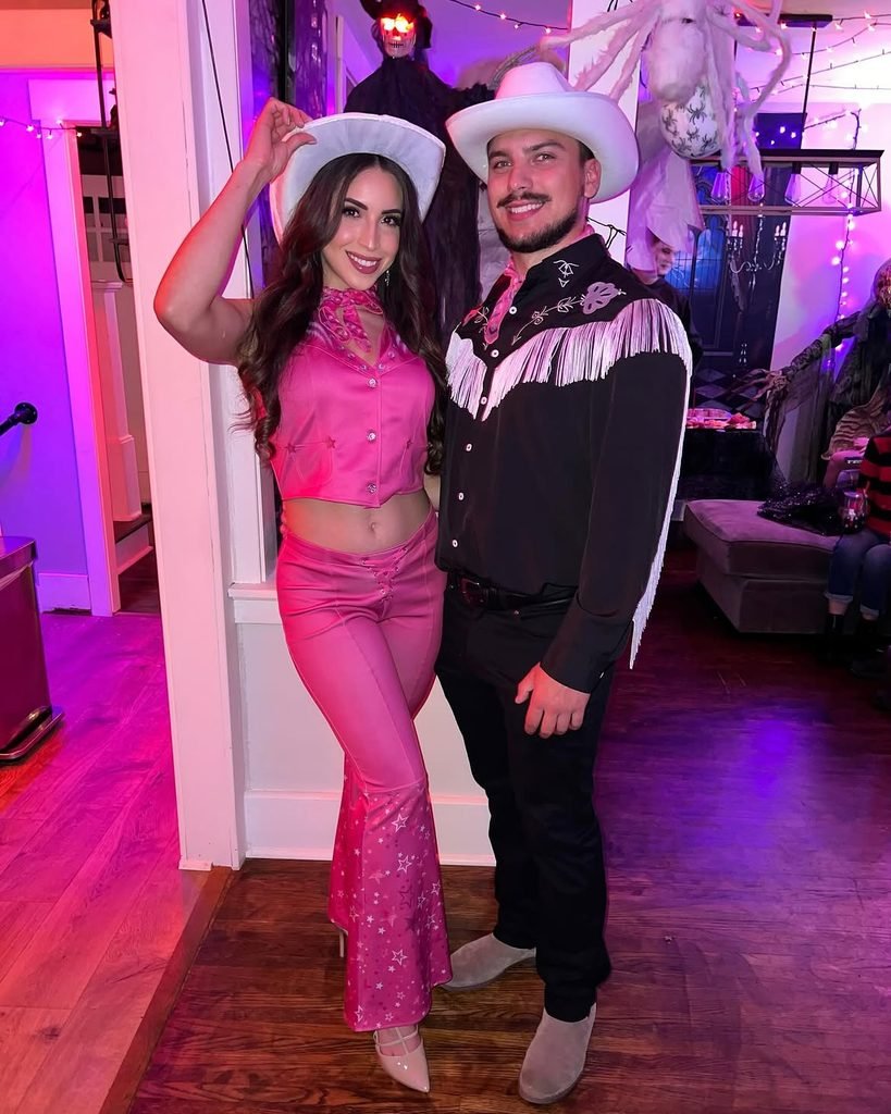 man and woman posing indoors dressed in matching pink and black western barbie costumes