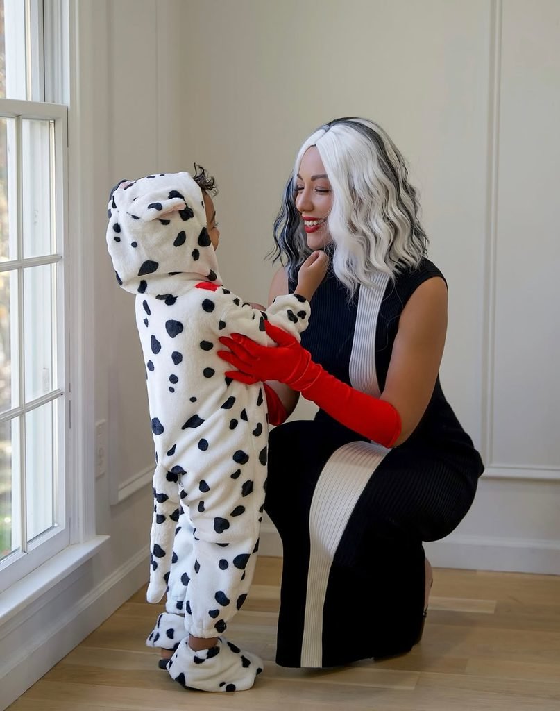 woman dressed as cruella de vil kneeling next to a toddler in a dalmatian costume