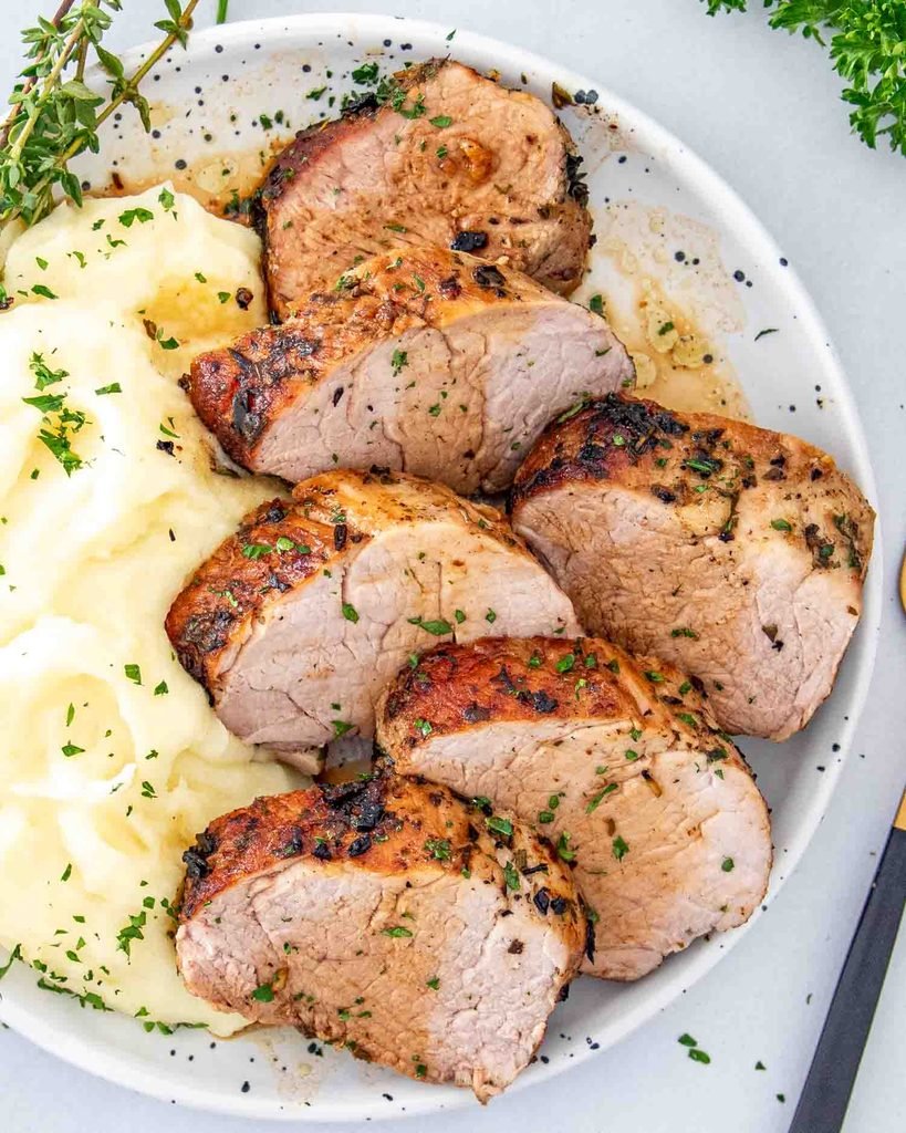 sliced herb crusted pork tenderloin served alongside creamy mashed potatoes   