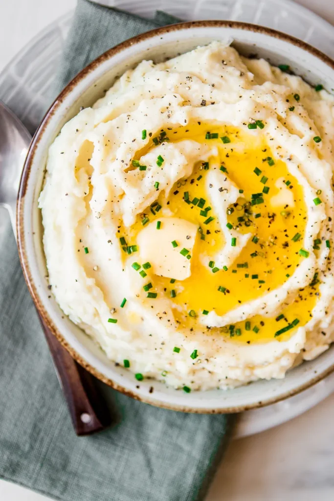 creamy garlic mashed potatoes topped with melted butter and fresh chives in a ceramic bowl   